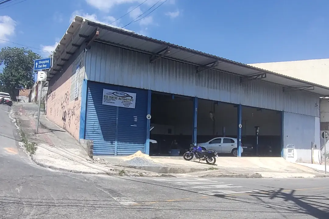 Fachada externa de um centro automotivo localizado em uma esquina, apresentando portões de aço na cor azul e recuo para a entrada e movimentação de veículos.